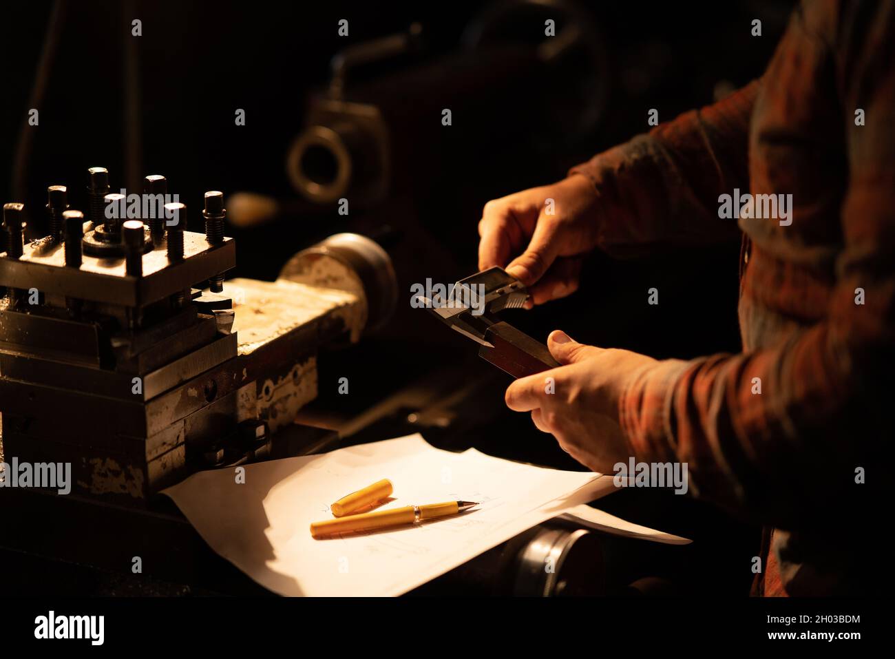 Primo piano di una mano industriale con calibro che misura la dimensione del componente in acciaio, all'interno di un'officina in metallo di notte. Foto Stock