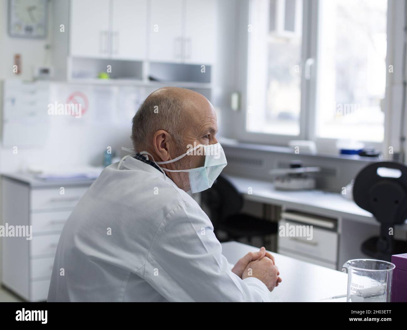 Medico senior con maschera protettiva seduta alla scrivania in laboratorio Foto Stock