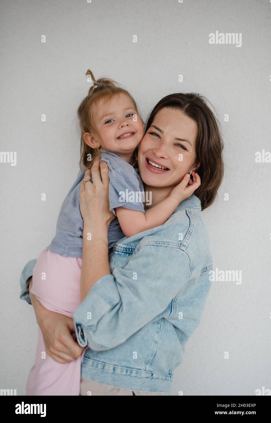 Ritratto di giovane madre felice con sua figlia abbracciante e guardando la macchina fotografica, su sfondo bianco. Foto Stock