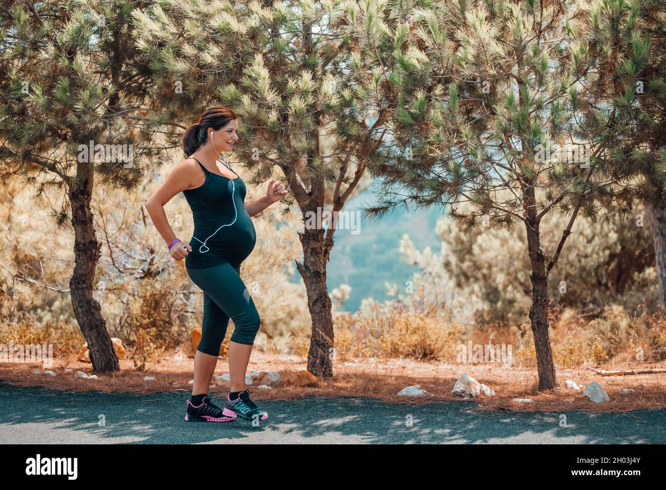 Cute donna incinta felice in allenamento nel Parco in giorno di sole. Goditi una passeggiata portiva tra splendidi alberi freschi. Gravidanza sana attiva. Foto Stock