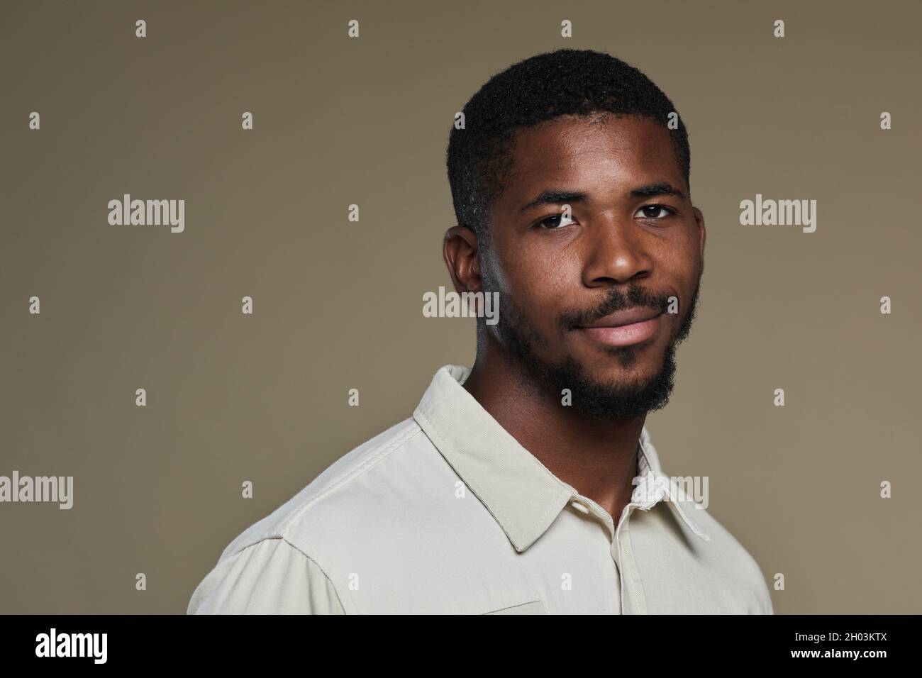 Ritratto minimale del giovane afroamericano che guarda la macchina fotografica e sorride mentre si posa su sfondo beige marrone neutro, spazio copia Foto Stock