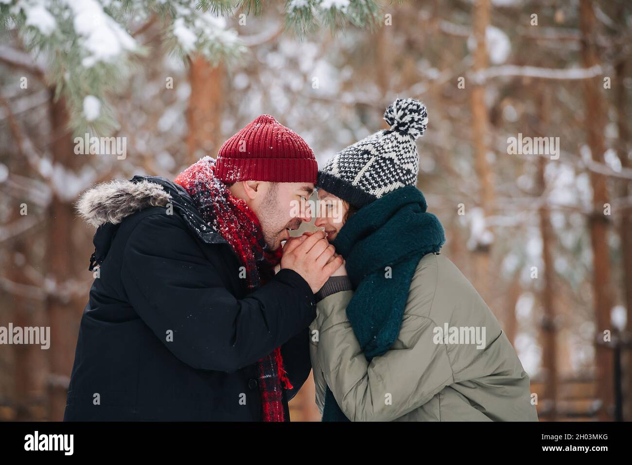Uomo attento che riscalda le mani della donna con il respiro. In un parco d'inverno Foto Stock
