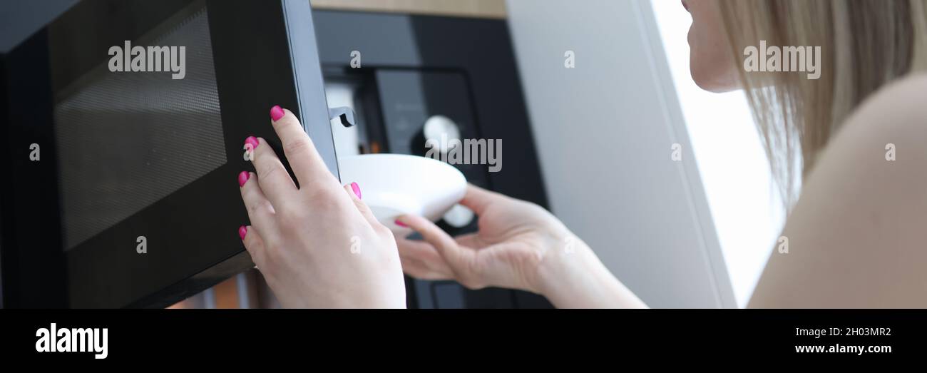 Donna che mette piatto bianco di cibo nel forno a microonde aperto Foto Stock