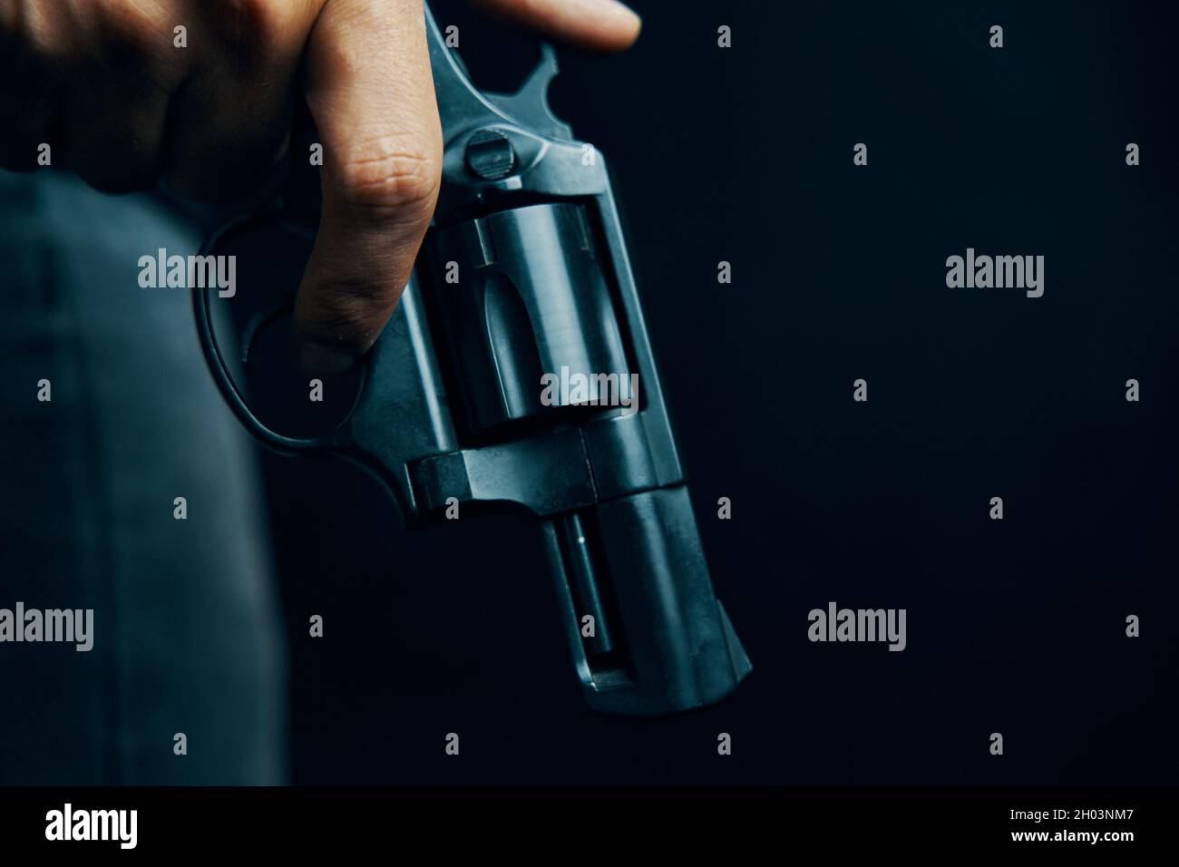 Revolver nero con tamburo in mano dell'uomo. Persona armata su sfondo scuro. Ragazzo con la pistola giù. Armi da fuoco per attacco o difesa. Foto Stock