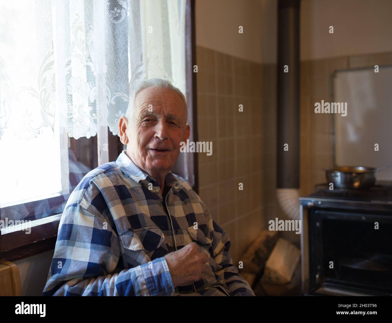 Ritratto di uomo anziano sorridente seduto accanto alla finestra in cucina d'epoca Foto Stock