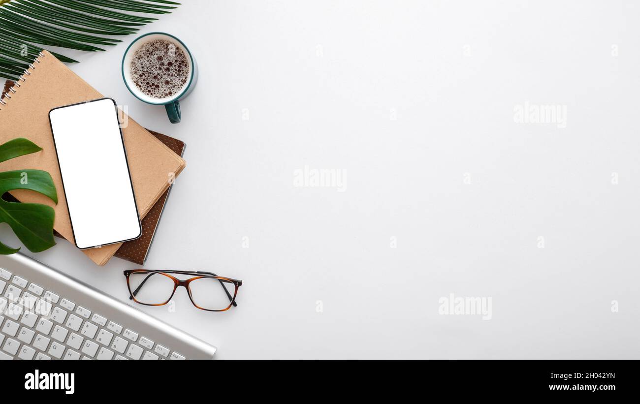 Lo schermo per smartphone si nota che i vetri della tastiera lasciano il palmo sulla scrivania bianca dello spazio di lavoro. Telefono cellulare su una moderna scrivania. Banner web lungo Foto Stock