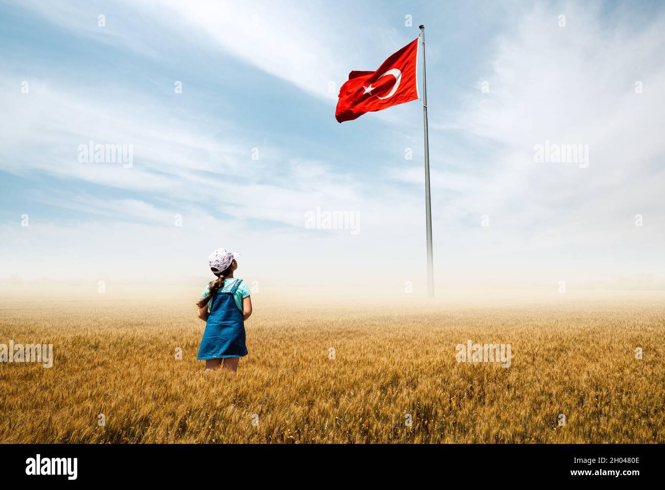 Adorabile bambina è in un campo con nebbia e guardando ammirevolmente alla bandiera nazionale turca. Foto di alta qualità Foto Stock