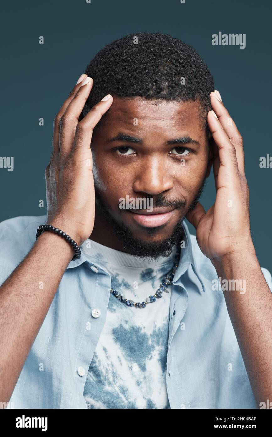 Ritratto verticale del bel giovane afroamericano che guarda la fotocamera sorridendo mentre si posa su sfondo blu Foto Stock