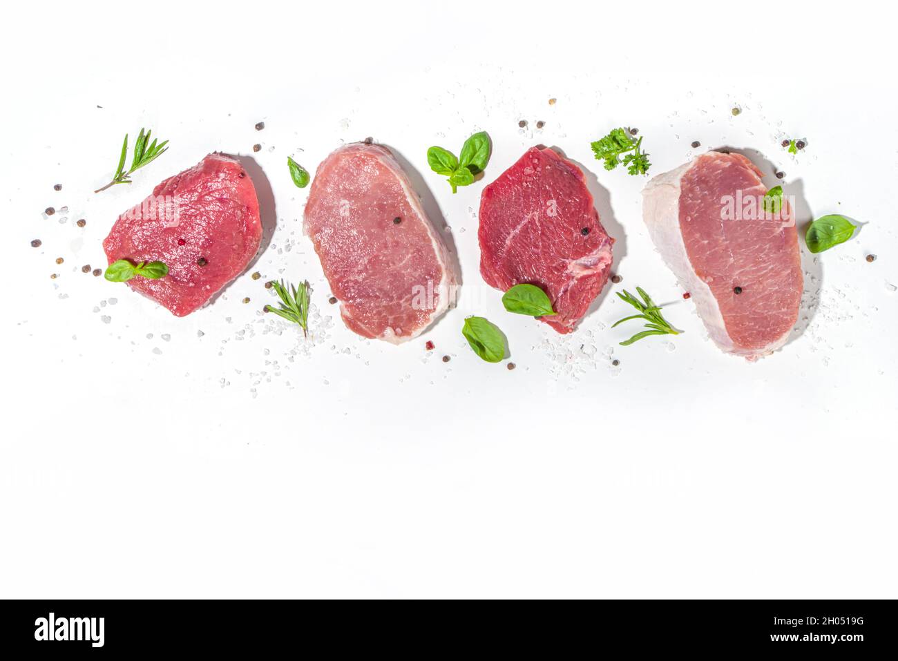 Pezzi di carne rossa assortiti, maiale crudo, agnello, bistecche di manzo, filetto di carne porzionato su sfondo di cemento scuro con spezie ed erbe per la cottura, vista dall'alto co Foto Stock