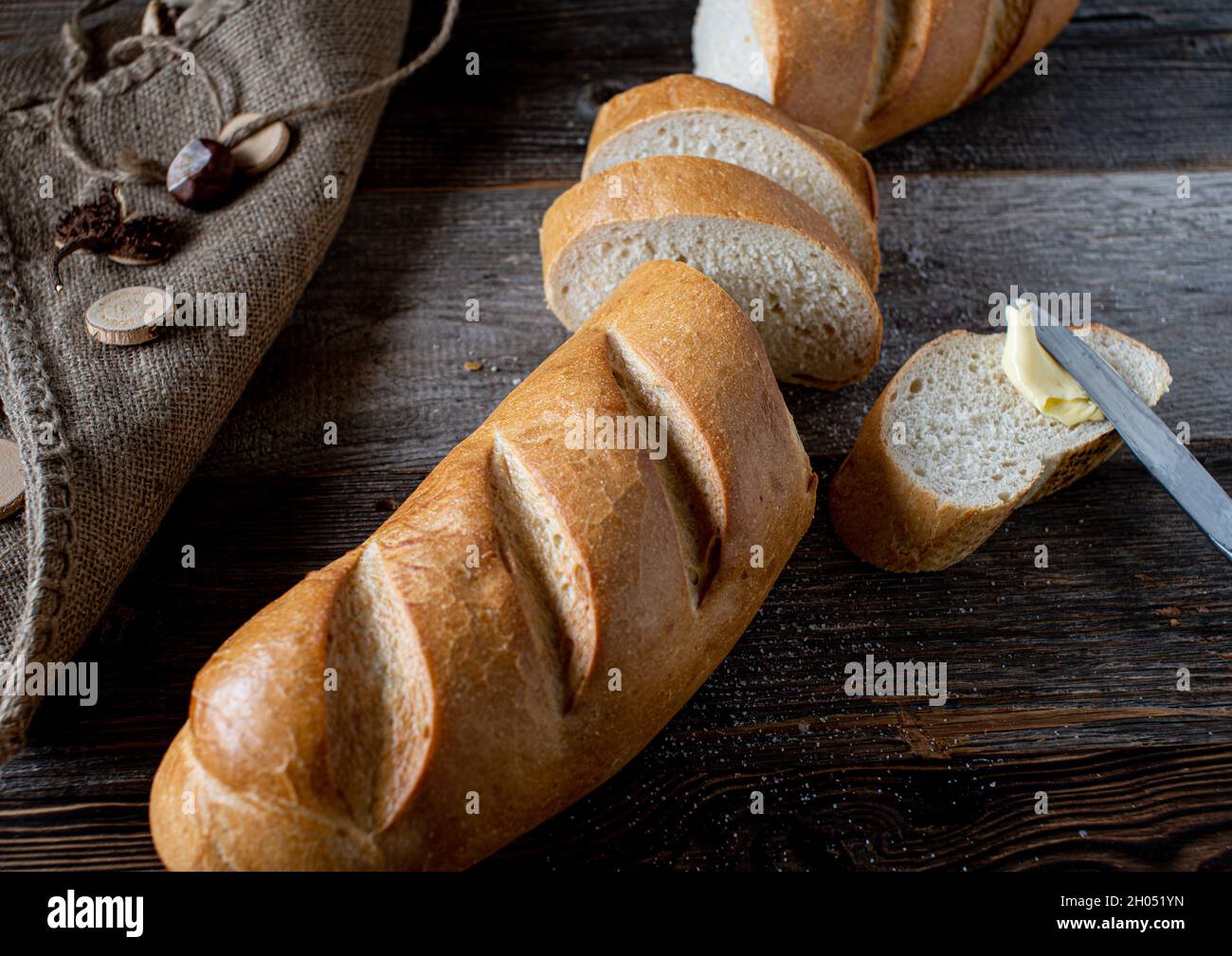 Baguette francese su tavola di legno con coltello e burro. Tagliate a pezzi e servite con un coltello di burro. Foto Stock