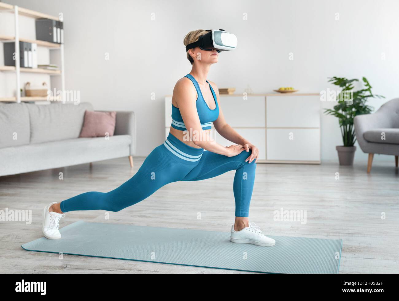 App VR Workout, gioco di fitness. Le cuffie sportive per la realtà vrtuale si esercitano utilizzando l'applicazione digitale, facendo il forward lunges a casa. Donna che usa m Foto Stock