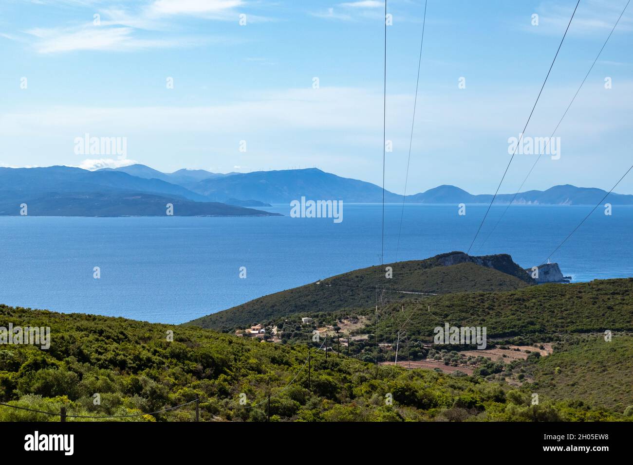 Paesaggio verde della costa dell'isola di Lefkada in Grecia con boschi verdi, cielo blu e linea elettrica di supporto. Infrastruttura energetica mediterranea Foto Stock