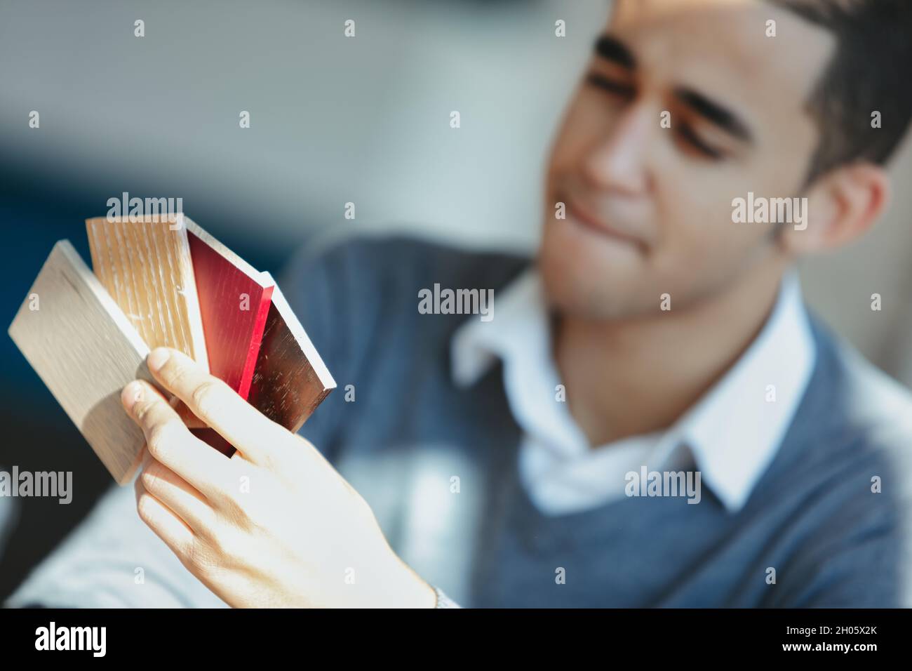 Uomo che sceglie tra diversi campioni di legno per arredamento d'interni che unisce il suo labbro in indecisione con fuoco ai campioni Foto Stock