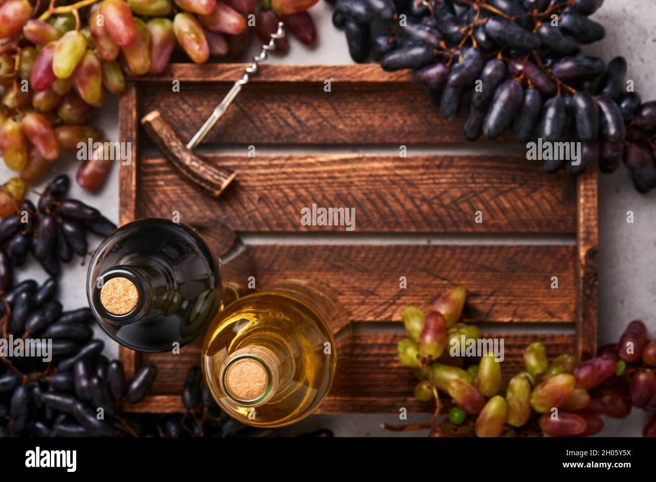 Due bottiglie di vino con uva e uva da vino su vecchio sfondo di tavola grigio cemento con spazio copia. Vino rosso con un ramo di vite. Composizione del vino su r Foto Stock