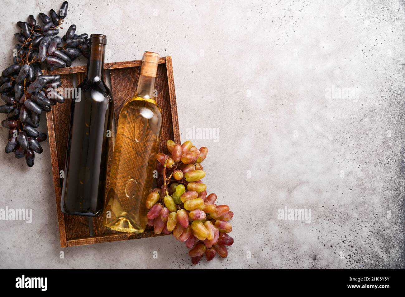 Due bottiglie di vino con uva e uva da vino su vecchio sfondo di tavola grigio cemento con spazio copia. Vino rosso con un ramo di vite. Composizione del vino su r Foto Stock