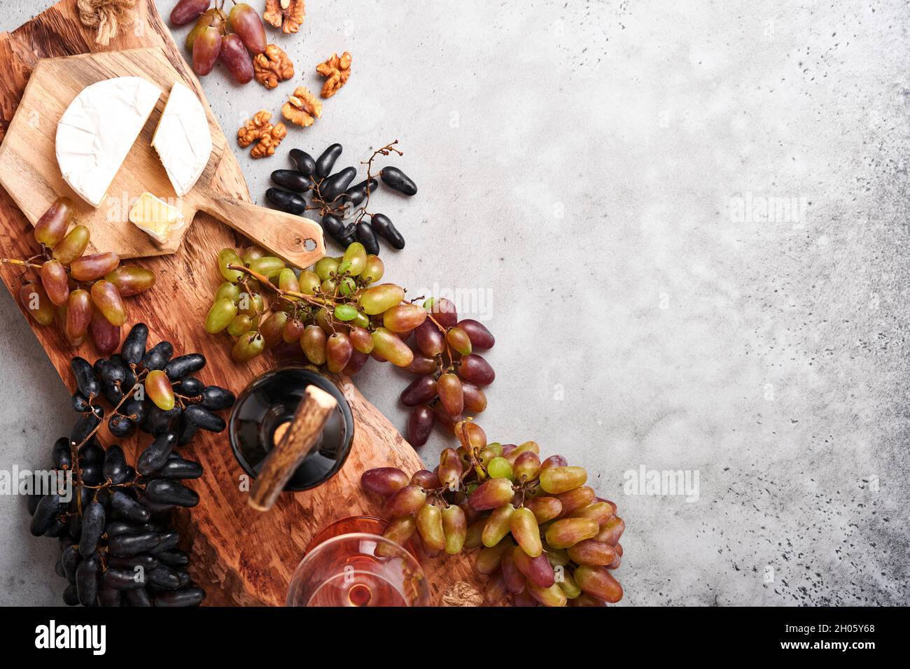 Due bottiglie di vino con uva, formaggio a fette camembert, noci e wineglasses su fondo vecchio tavolo grigio cemento con spazio copia. Vino rosso con vite br Foto Stock