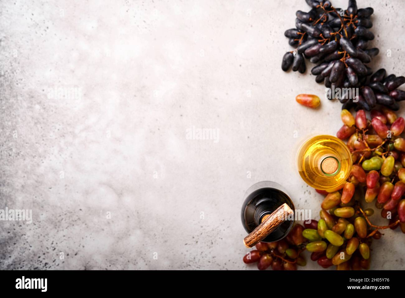 Bottiglie di vino con uva e vinacce su vecchio fondo di tavola grigio cemento con spazio copia. Vino rosso con un ramo di vite. Composizione del vino su rusti Foto Stock