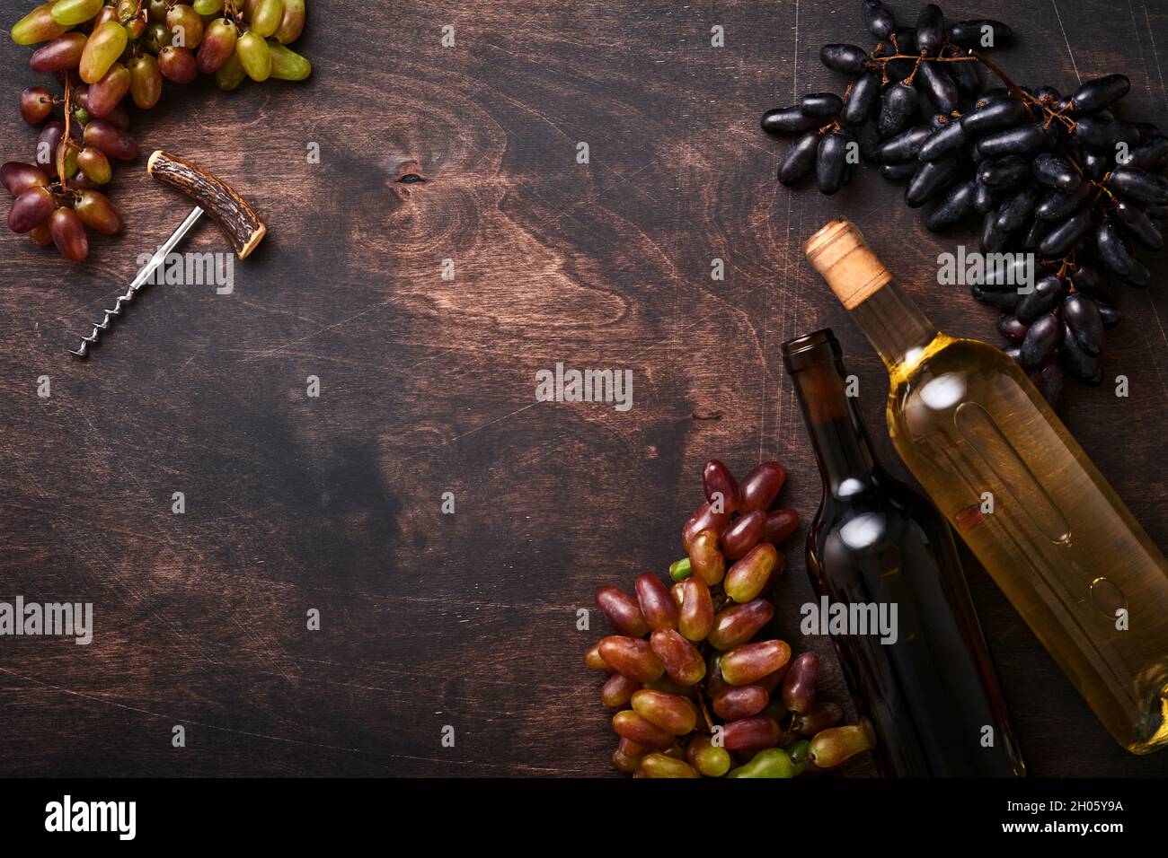 Bottiglie di vino con uva e vineglasses su vecchio sfondo di tavola di legno scuro con spazio copia. Vino rosso con un ramo di vite. Composizione del vino su rustico Foto Stock