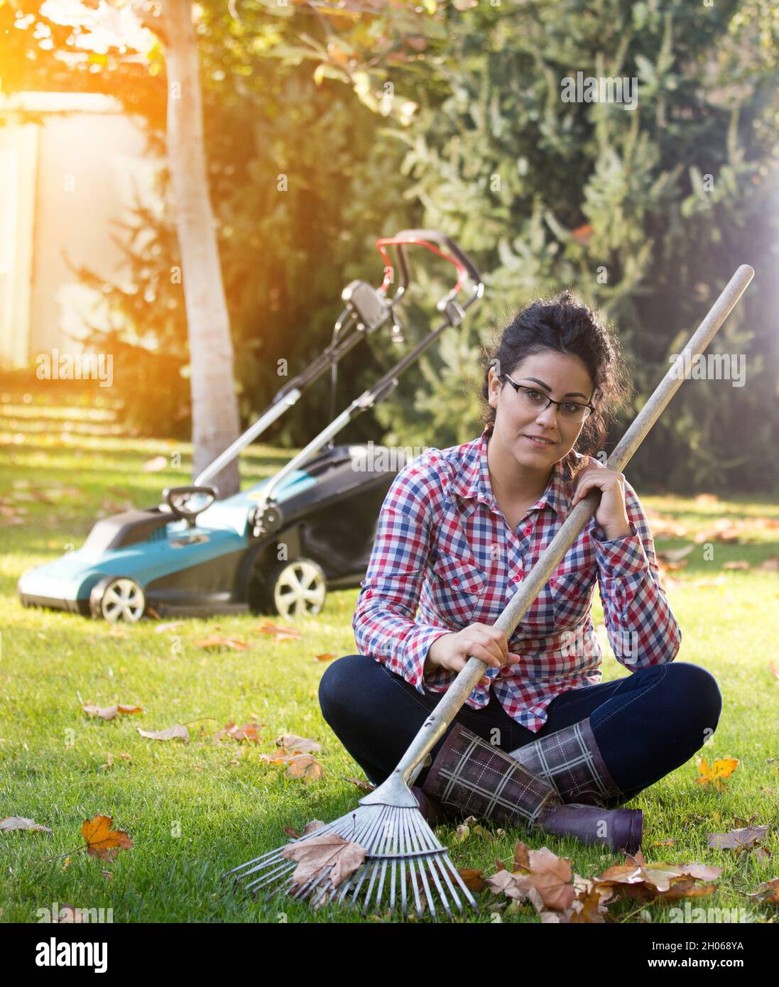 Donna piuttosto giovane che riposa sull'erba dopo aver rastrellato le foglie e aver falciato il prato in autunno Foto Stock