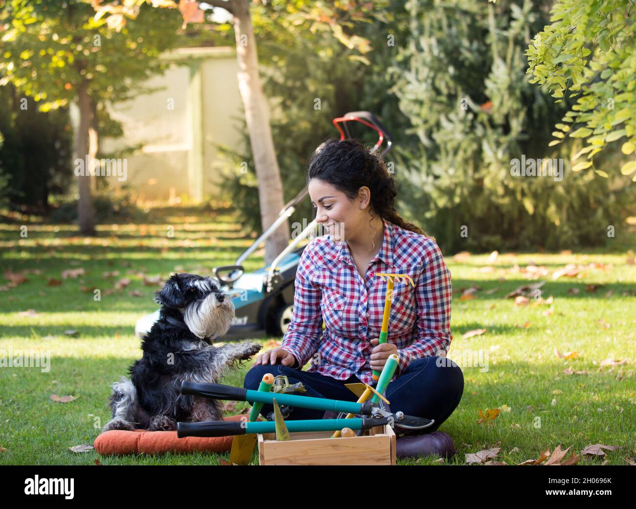 Bella giovane donna e cane seduto sul prato in cortile. Attrezzi di giardinaggio di tenuta Foto Stock