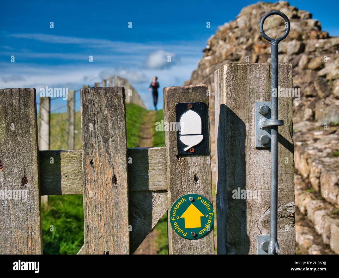Un corridore lontano si avvicina a un cancello contrassegnato con i segni del sentiero sul percorso nazionale del Vallo di Adriano nel Northumberland, Regno Unito. In una giornata di sole wi Foto Stock