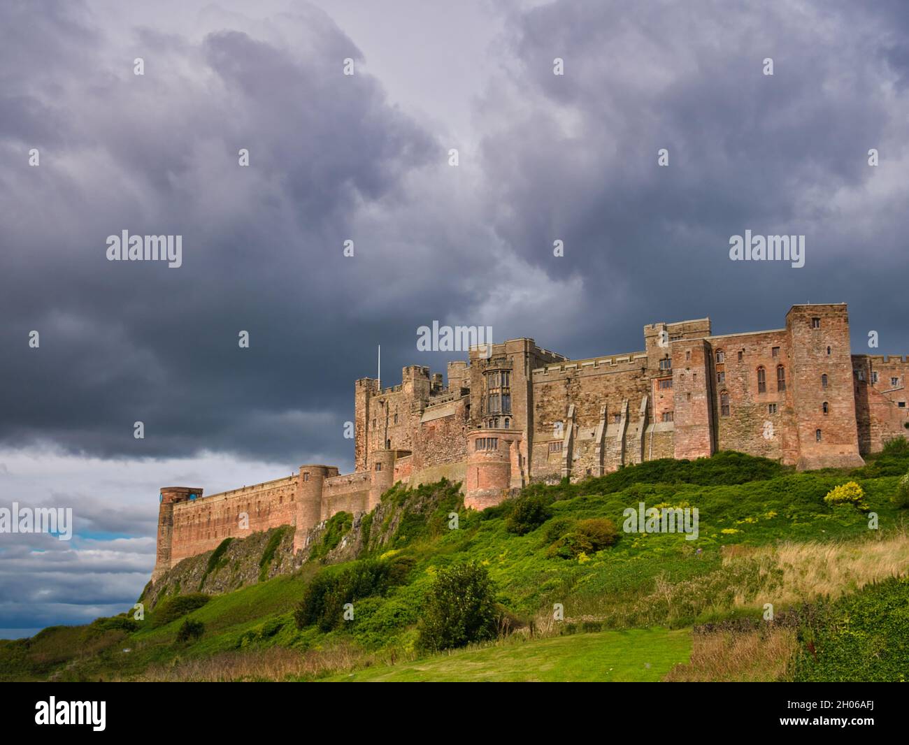 Con il sole che brilla attraverso nuvole minacciose, il lato sud-occidentale della fortezza dell'edificio classificato di grado 1, il Castello di Bambburgh nel Northumberland, Regno Unito Foto Stock