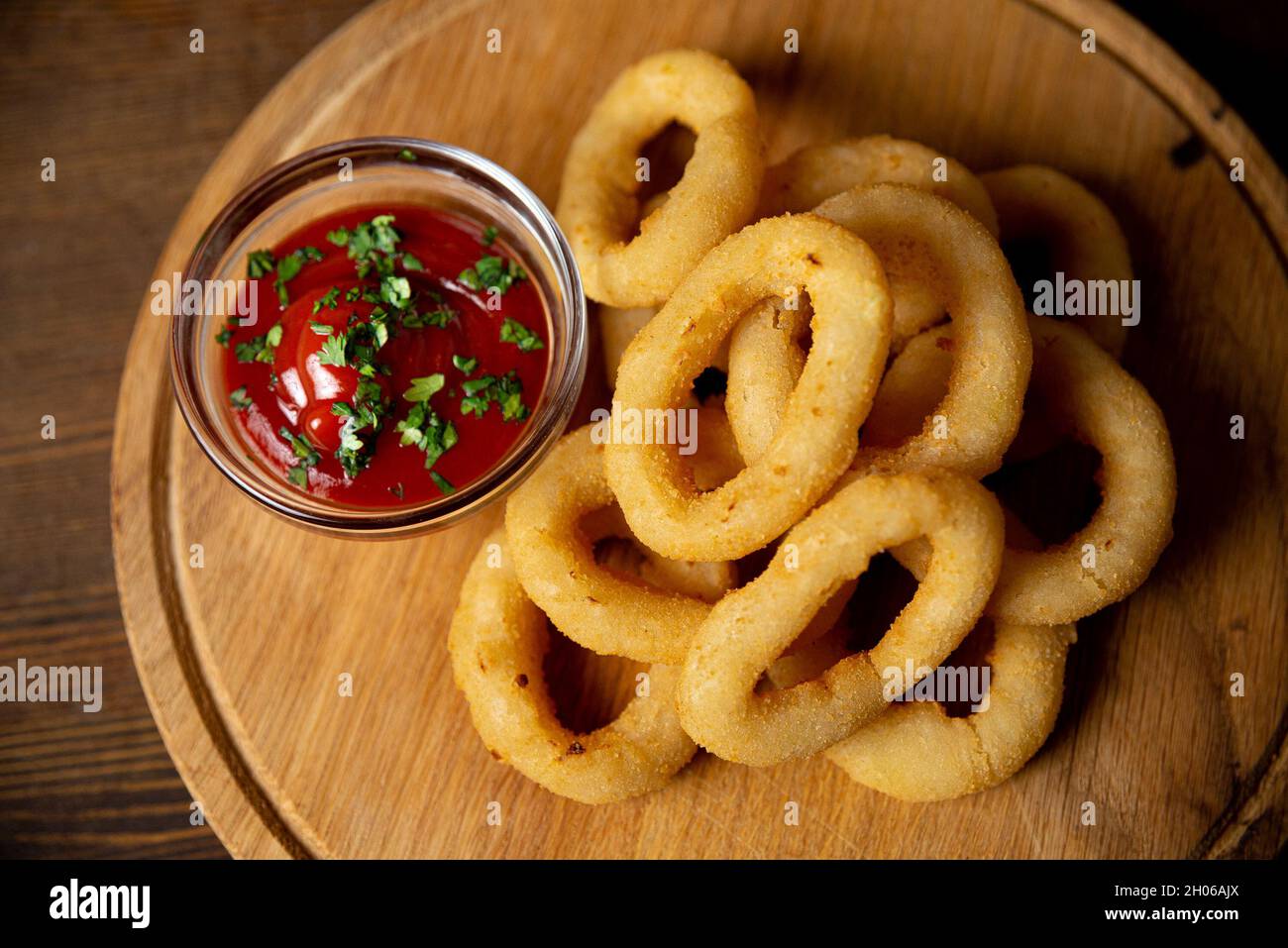 Anelli di cipolla con ketchup su un tagliere di legno. Cibo da bar. Un servizio a persona. Cospargere con pepe macinato. Un piccolo mazzo di anelli di cipolla. Foto Stock