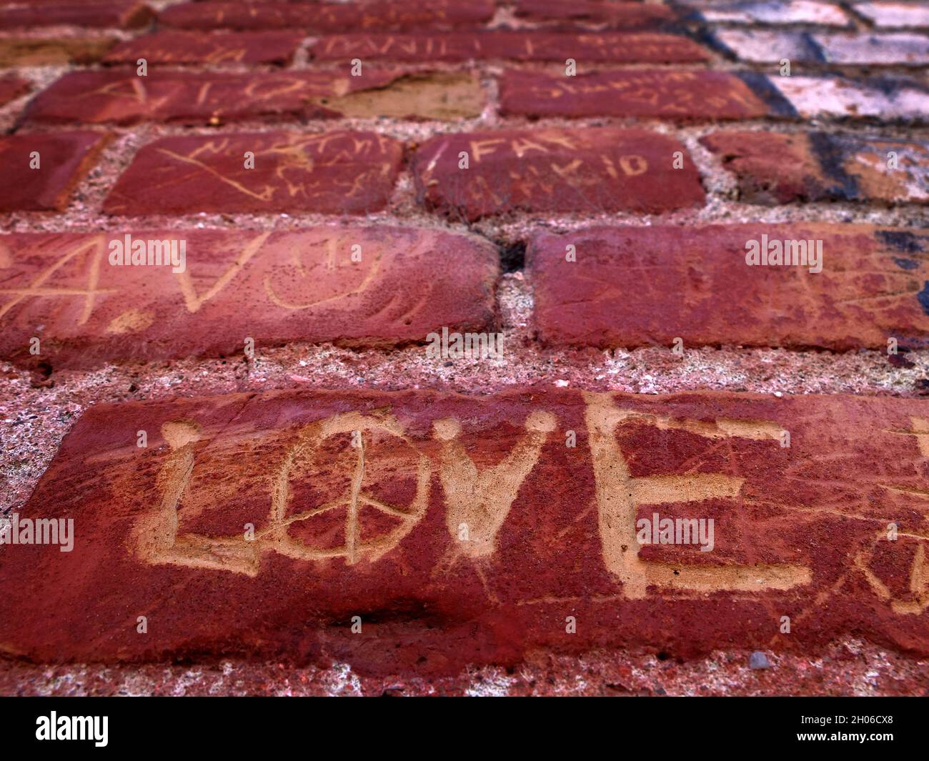 Dettaglio del vecchio muro di mattoni rossi con le parole nomi e l'amore graffiato o scolpito in Foto Stock