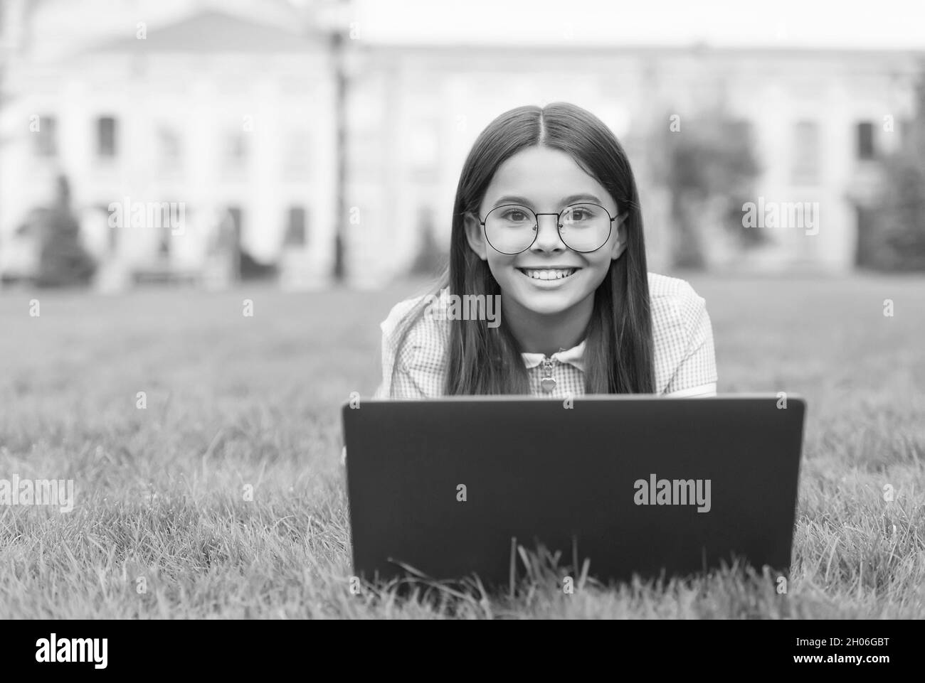 Vera felicità. Ragazza felice seduta su erba verde con laptop. Avvio. Bambino che gioca al computer. Torna a scuola. Formazione online. Giornata della conoscenza Foto Stock