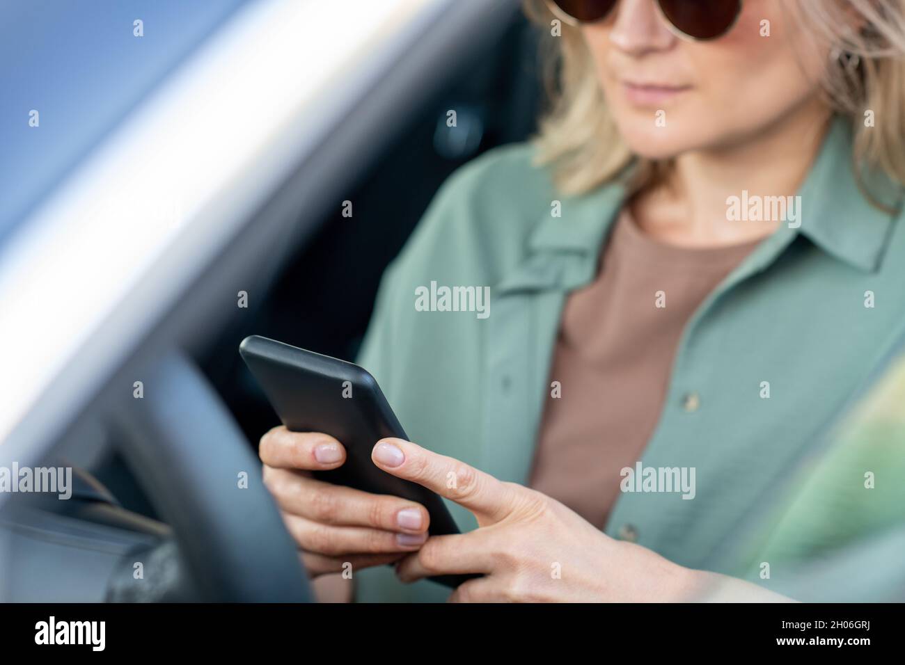 Mani di elegante scorrimento femminile in smartphone mentre si siede al volante in auto Foto Stock