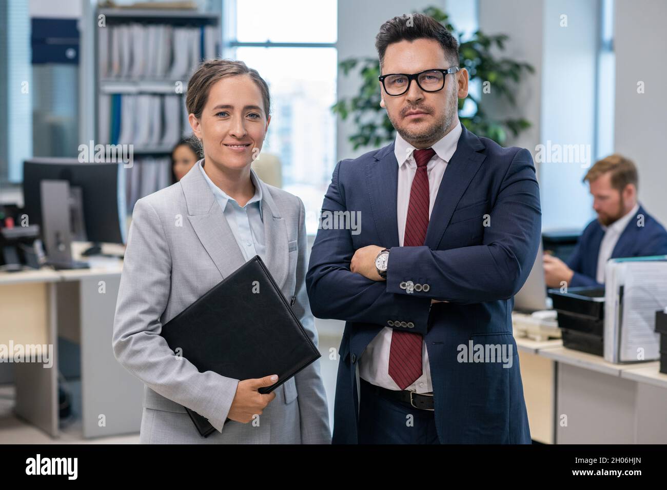 Due dipendenti ben vestiti che si trovano di fronte alla fotocamera in ufficio Foto Stock