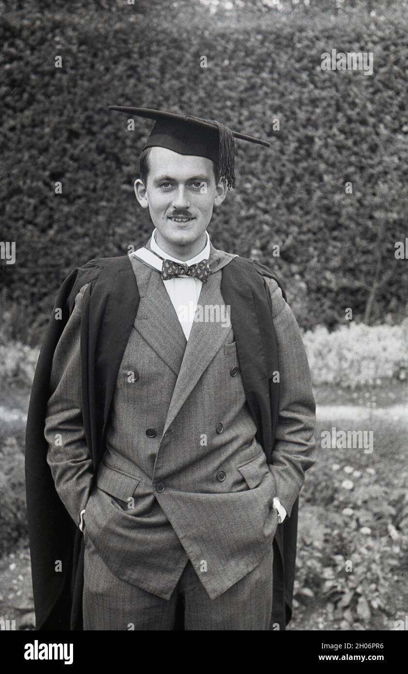 Anni '50, storico, un giovane inglese con un baffo corto e indossando un abito a doppia prora e una cravatta ad arco in posa per la sua foto in un abito da laurea e cappellino accademico quadrato, spesso definito come cappellino e abito, Inghilterra, Regno Unito. Indossato con regalia accademica alle cerimonie di laurea, il suo tipo speciale di cappellino è noto come un mortarboard o a volte come cappellino Oxford e consiste di una tavola quadrata orizzontale fissata su un cappellino cranio con un tasello attaccato al centro. Il suo aspetto distintivo significa che la PAC è associata al mondo accademico. Foto Stock