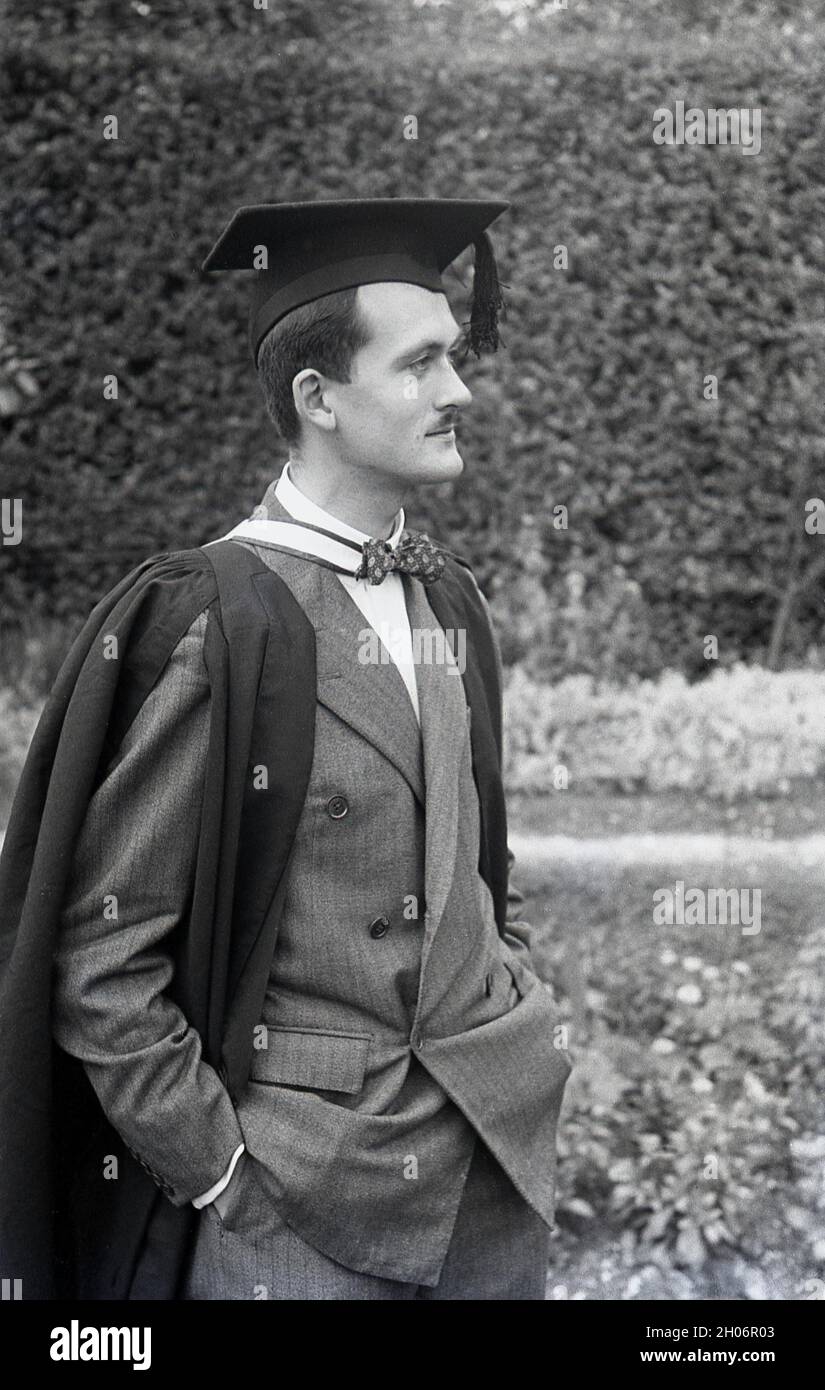 Anni '50, storico, un giovane inglese con un baffo corto e indossando un abito a doppia prora e una cravatta ad arco in posa per la sua foto in un abito da laurea e cappellino accademico quadrato, spesso definito come cappellino e abito, Inghilterra, Regno Unito. Indossato con regalia accademica alle cerimonie di laurea, il suo tipo speciale di cappellino è noto come un mortarboard o a volte come cappellino Oxford e consiste di una tavola quadrata orizzontale fissata su un cappellino cranio con un tasello attaccato al centro. Il suo aspetto distintivo significa che la PAC è associata al mondo accademico. Foto Stock