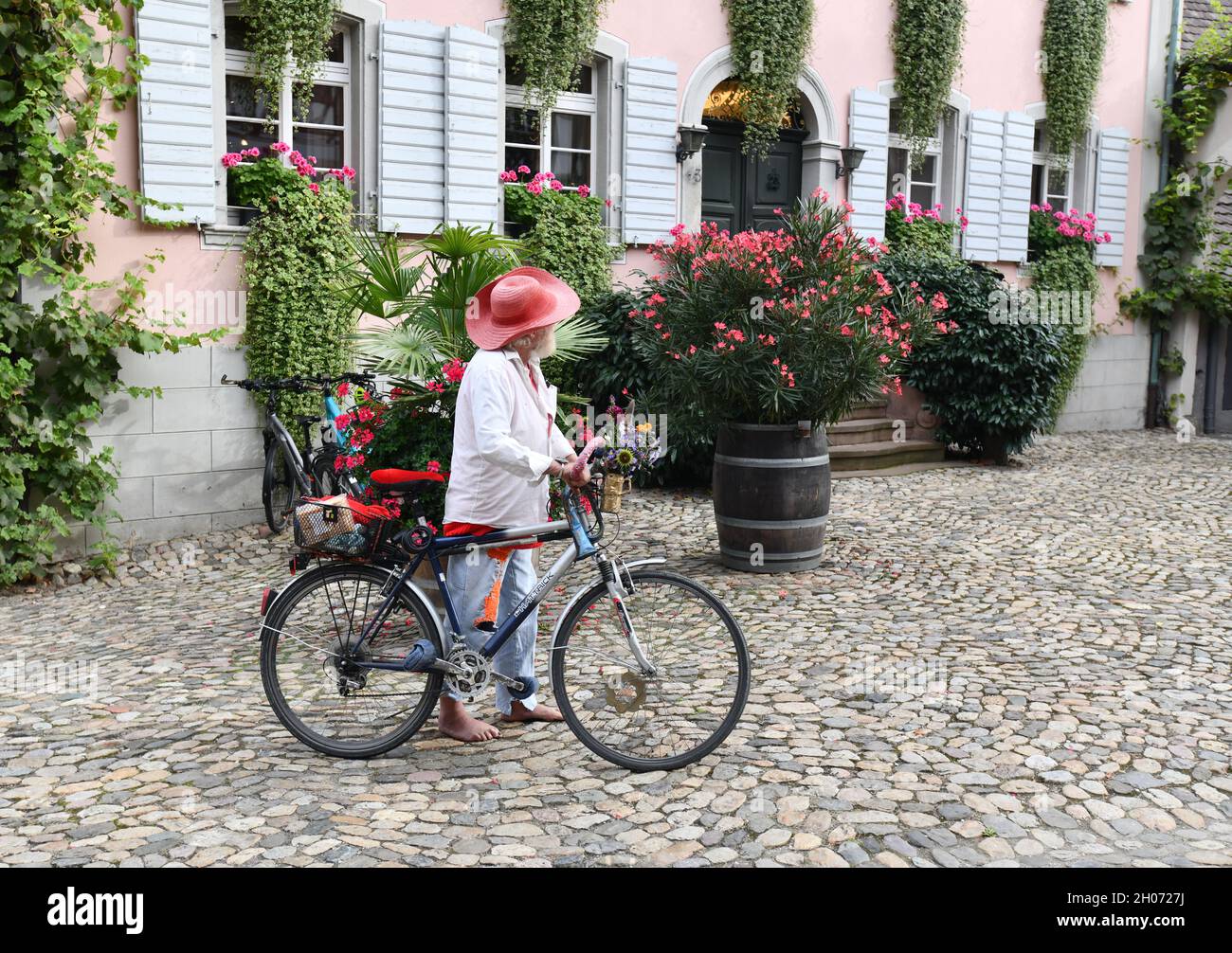 Uomo anziano colorato camminando a piedi nudi con la sua bicicletta decorata nel villaggio di Burkheim Germania. Flamboyant, stilismo, elegante, Foto Stock