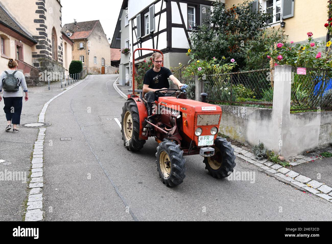Giovane agricoltore tedesco che guida un piccolo trattore attraverso il villaggio di Burkheim Germania durante la vendemmia. Germania Foto Stock