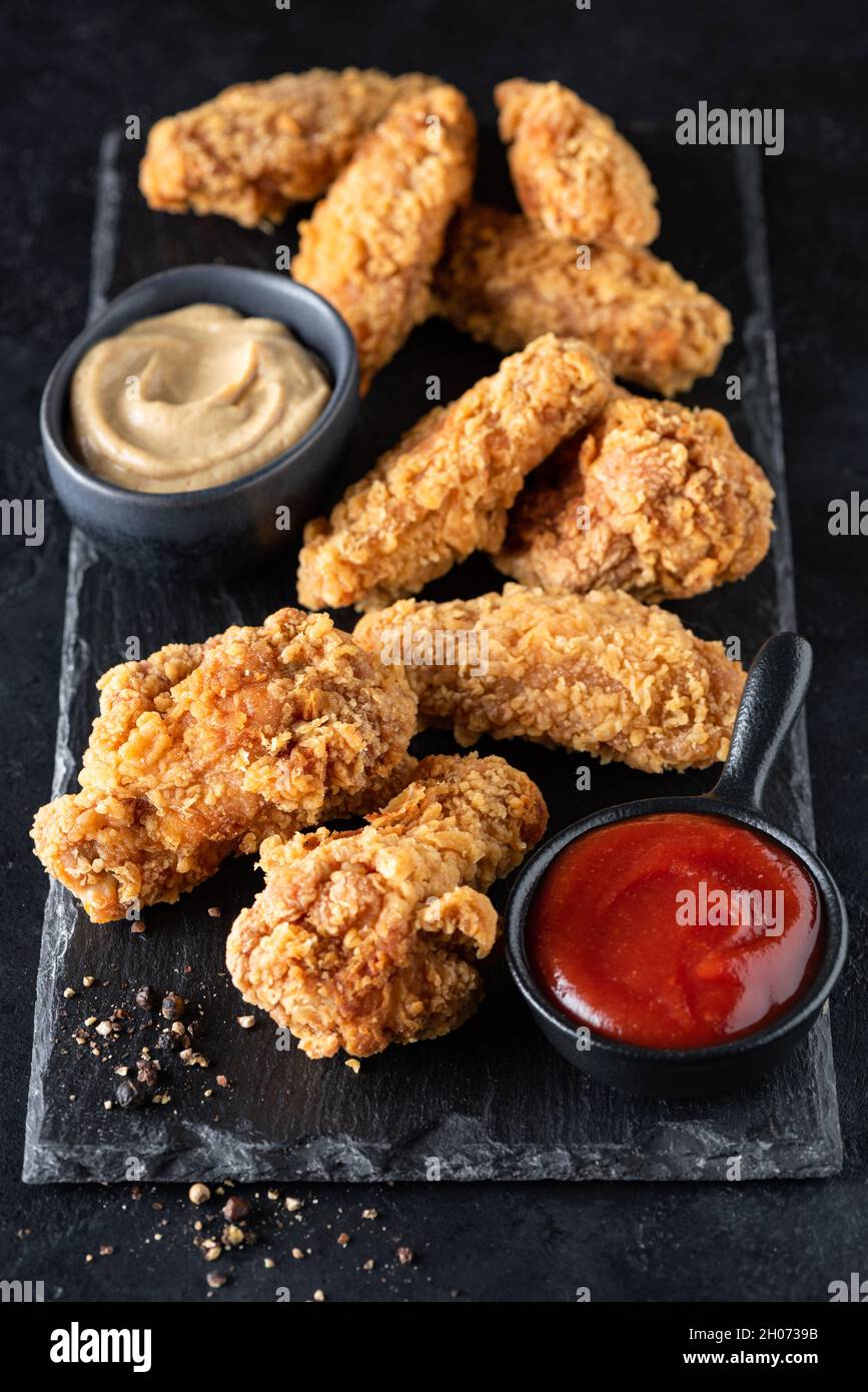 Ali di pollo speziate e fritte con salse servite su ardesia nera. Cibo spazzatura Foto Stock