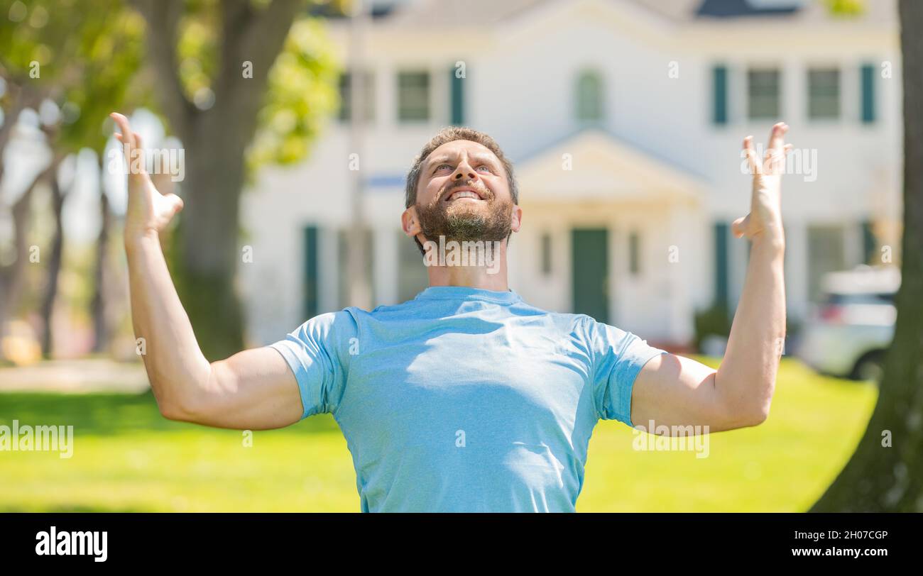 felice unshaven ragazzo in piedi vicino casa nuova celebrando il successo, nuova casa Foto Stock