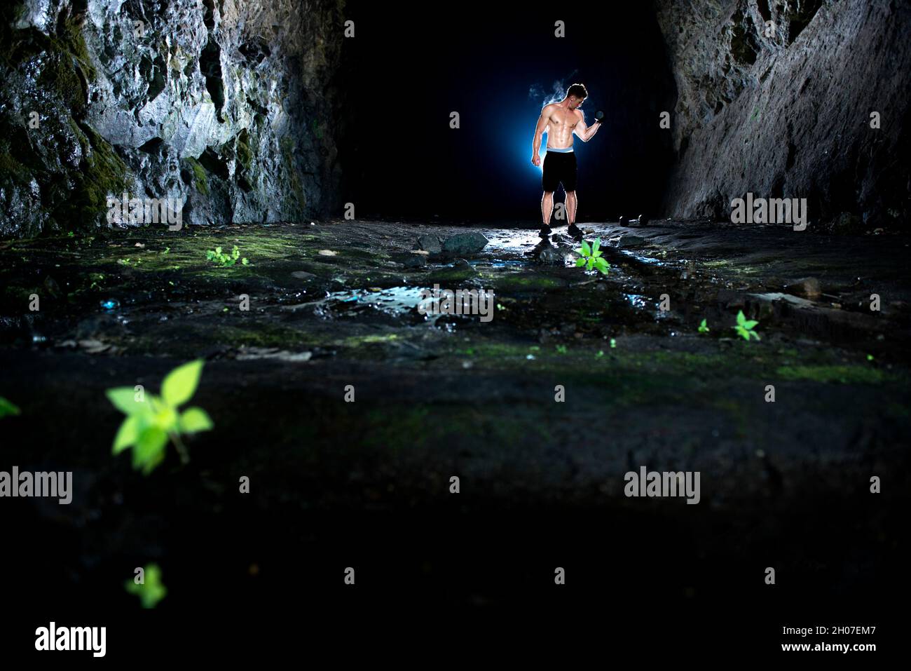 Forte giovane maschio sollevamento manubri in una grotta Foto Stock