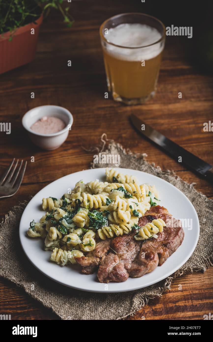 Bistecca di maiale fritta e pasta di spinaci con ricotta e parmigiano Formaggio su piatto bianco Foto Stock