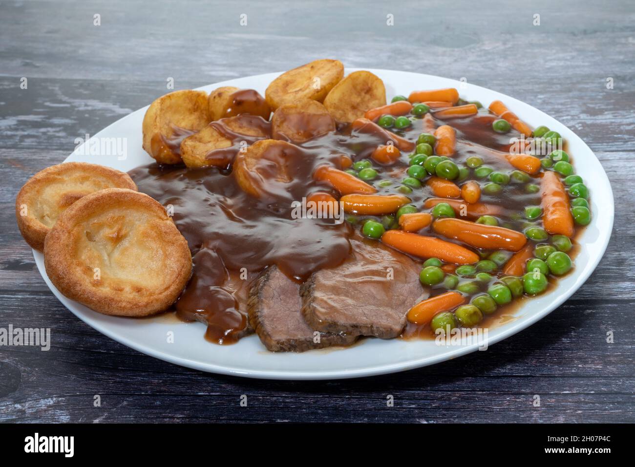 Cena di manzo arrosto con sugo di carne con piselli, carote, patate arrosto e budini dello Yorkshire Foto Stock