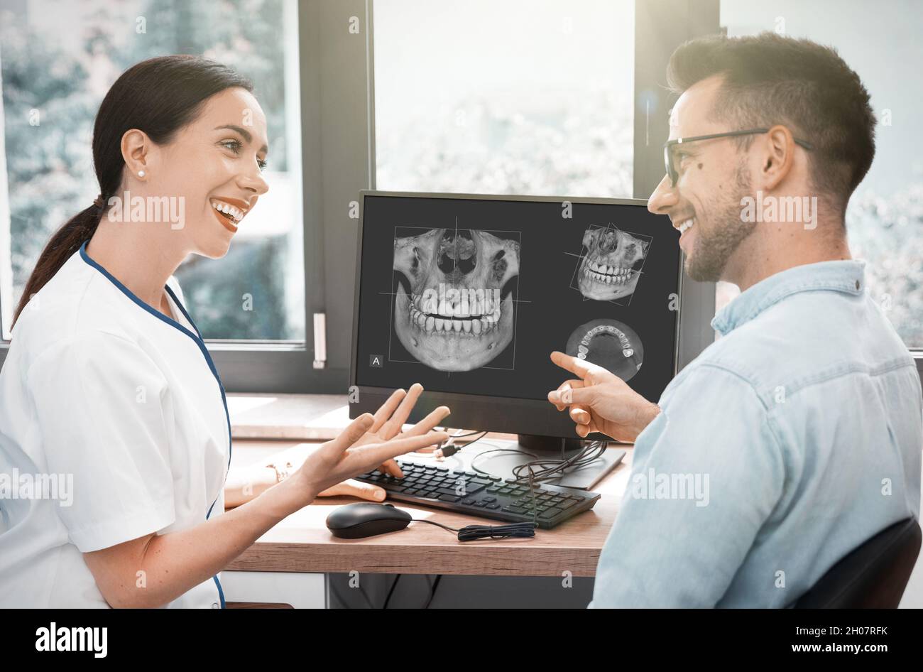 Il dentista e il paziente scelgono il trattamento in consultazione con la moderna immagine a raggi X 3D sullo schermo Foto Stock