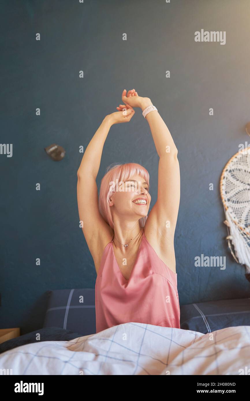 Donna gioiosa in elegante pigiama tende a svegliarsi in grande letto al mattino pigro Foto Stock