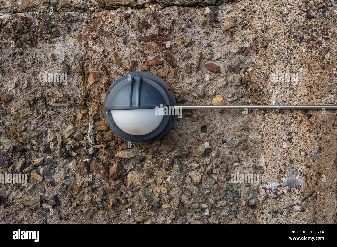 Applique esterna a parete con tenuta stagna fissata troppo a una parete in calcestruzzo e a un condotto elettrico in acciaio inox. Foto Stock