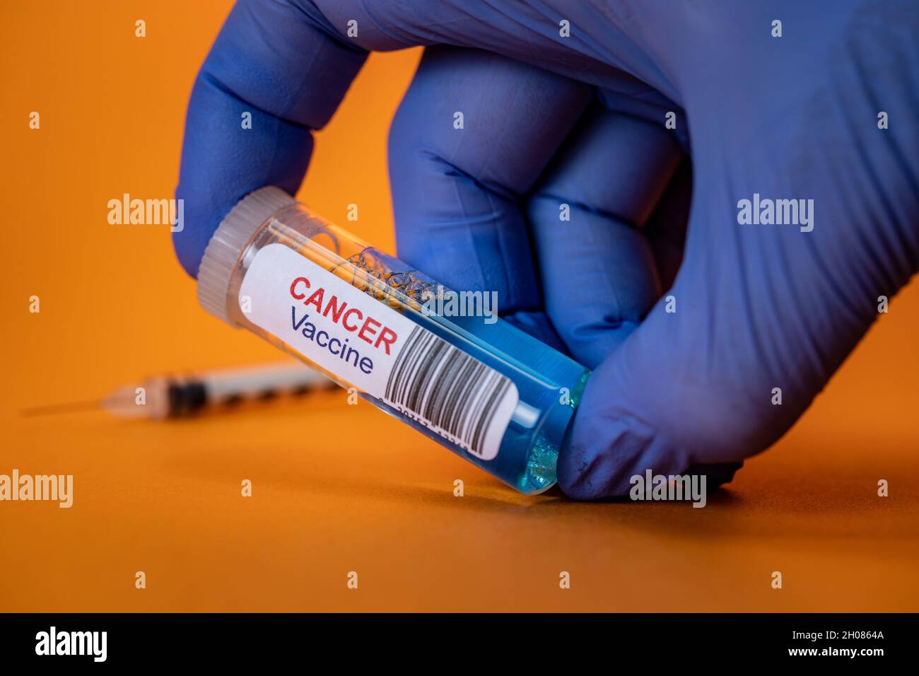 Vaccino antitumorale gloved Hand Holding con siringa su sfondo arancione Foto Stock