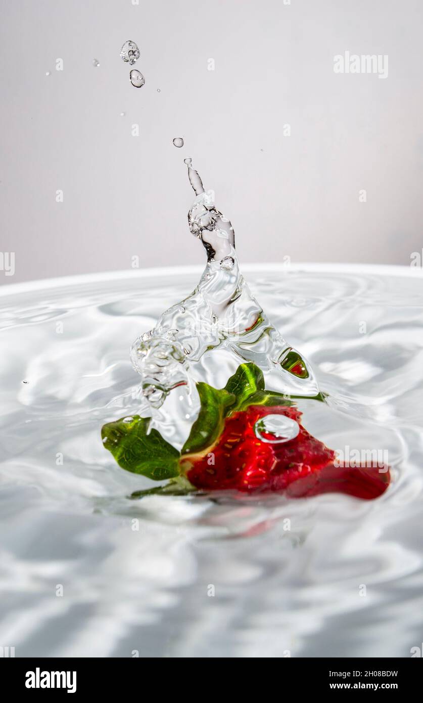 Getto d'acqua creato da una fragola che cade in acqua Foto Stock
