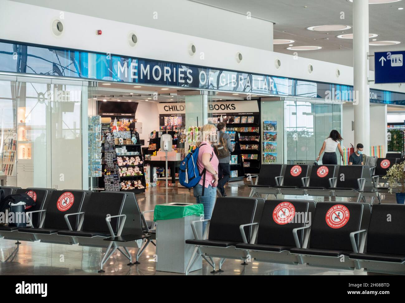 Parte della sala passeggeri dell'aeroporto di Gibilterra che presenta i  ricordi del negozio di souvenir di Gibilterra. Alcuni passeggeri che  indossano maschere si trovano nella zona Foto stock - Alamy