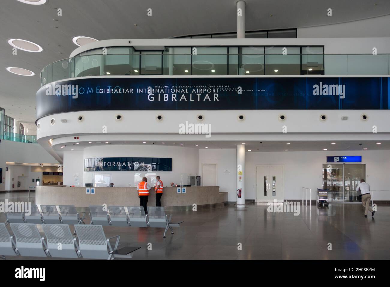 Un'area d'attesa quasi vuota all'interno dell'ingresso dell'aeroporto internazionale di Gibilterra, con un cartello di benvenuto e un banco informazioni. Foto Stock