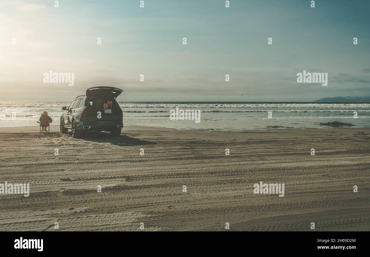 Donna nei suoi 40s godendo posto a sedere di Beach Place da solo accanto alla sua auto pieno di bagaglio. Spostamento a Better Place Conceptual Photo. Foto Stock