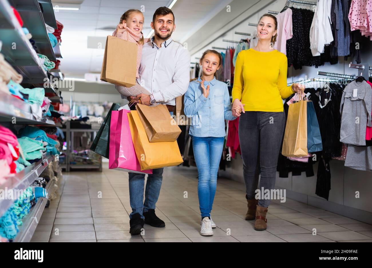 Giovani genitori felici con due bambine che acquistano nel centro commerciale, portando acquisti Foto Stock