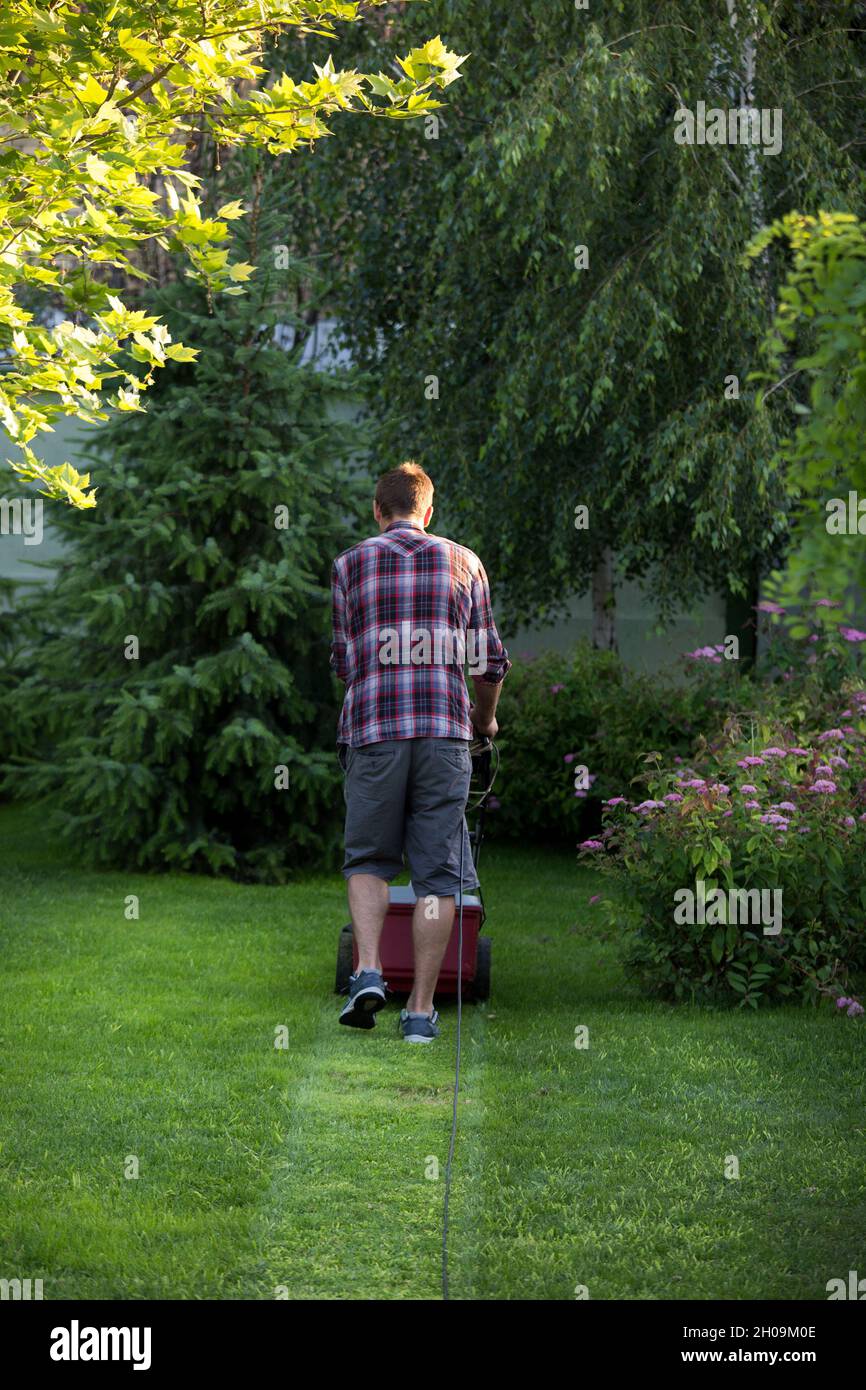 Vista posteriore del bel giovane uomo che rifilatura erba con il rasaerba elettrico in giardino Foto Stock
